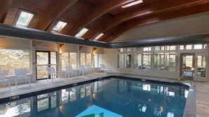 Une piscine intérieure avec une pancarte indiquant « Seasons on Mount Snow », un plafond en bois et de grandes fenêtres baignées de lumière.