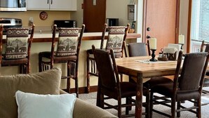 Un coin repas avec une table et des chaises en bois, un lustre et une cuisine en arrière-plan.