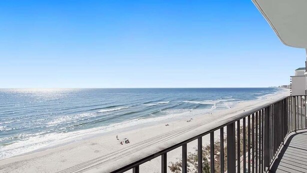 Blick auf den Strand vom Balkon mit Geländer, Meer und Badegäste.