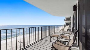 Ein Balkon mit Blick auf Strand und Meer. Auf dem Balkon stehen Stühle und ein Tisch.