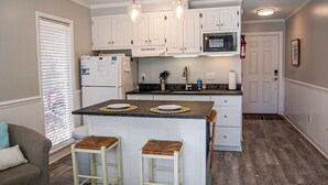 Una cocina con armarios blancos, una isla central con taburetes, microondas y refrigerador.