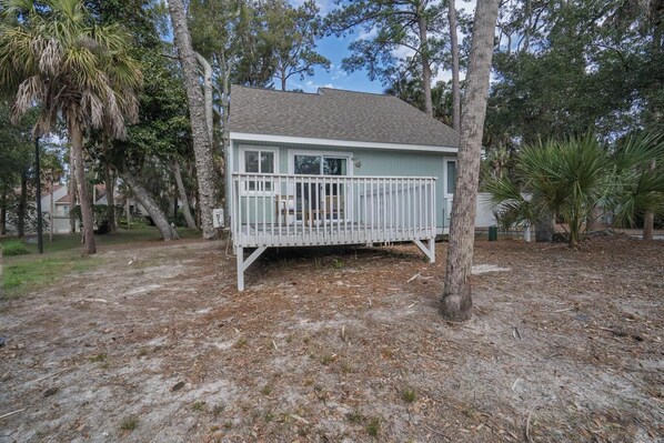 A small, single-story house with a white porch and a covered deck area.