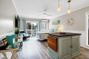 A spacious living area with a large sliding glass door leading to a balcony, a central island with a sink, and a ceiling fan.