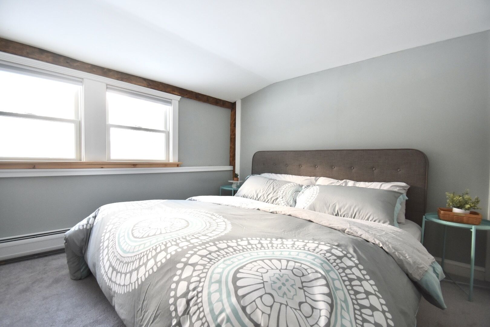 A bedroom with a large bed, a window, and a nightstand with a plant.