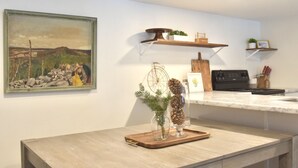 Een keuken met een marmeren aanrecht, houten planken, een schilderij en een decoratieve decoratie van dennenappels.