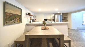 Een moderne keuken met witte kasten, een roestvrijstalen koelkast en een houten eettafel met bankjes.