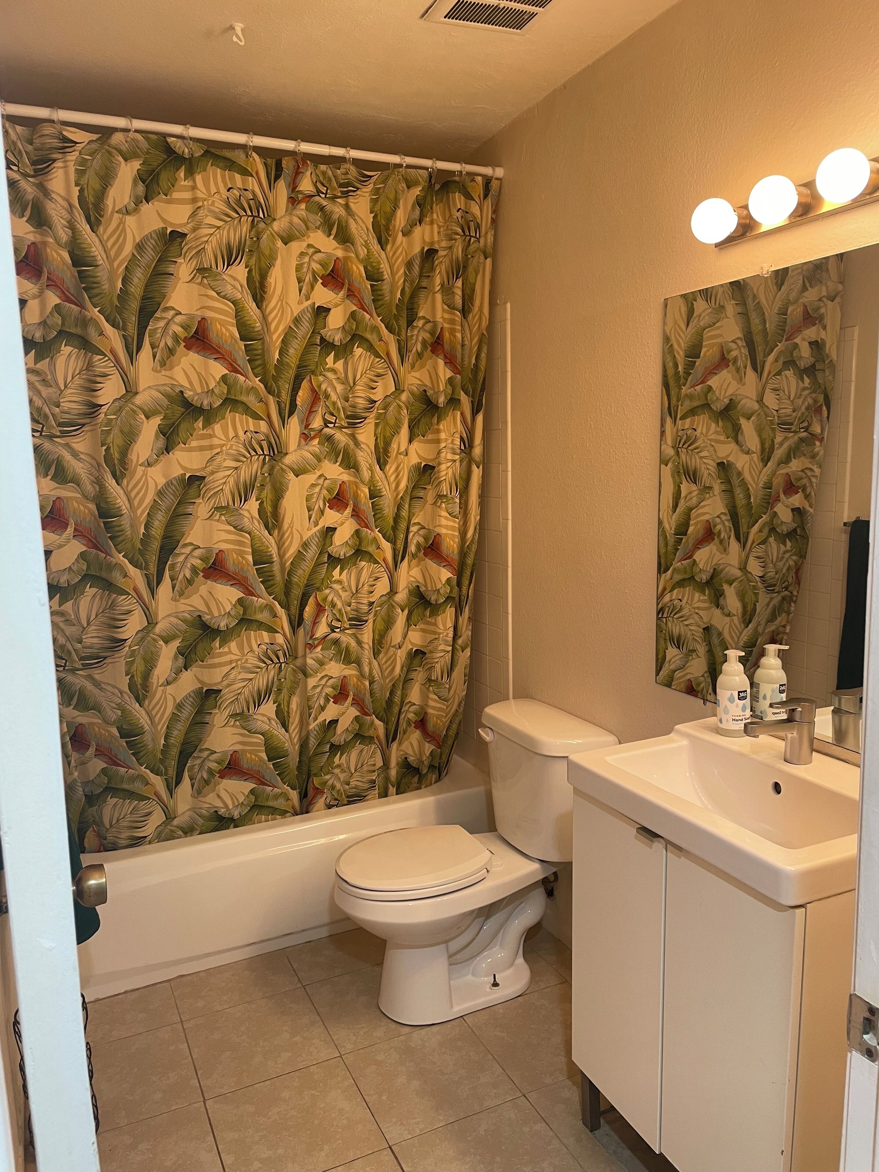 A bathroom with a toilet, sink, and shower curtain with a tropical leaf pattern.