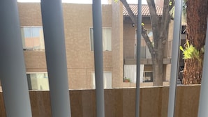 Ein Balkon mit rundem Tisch und zwei gemusterten Stühlen, im Hintergrund ein Gebäude und rechts ein Baum.