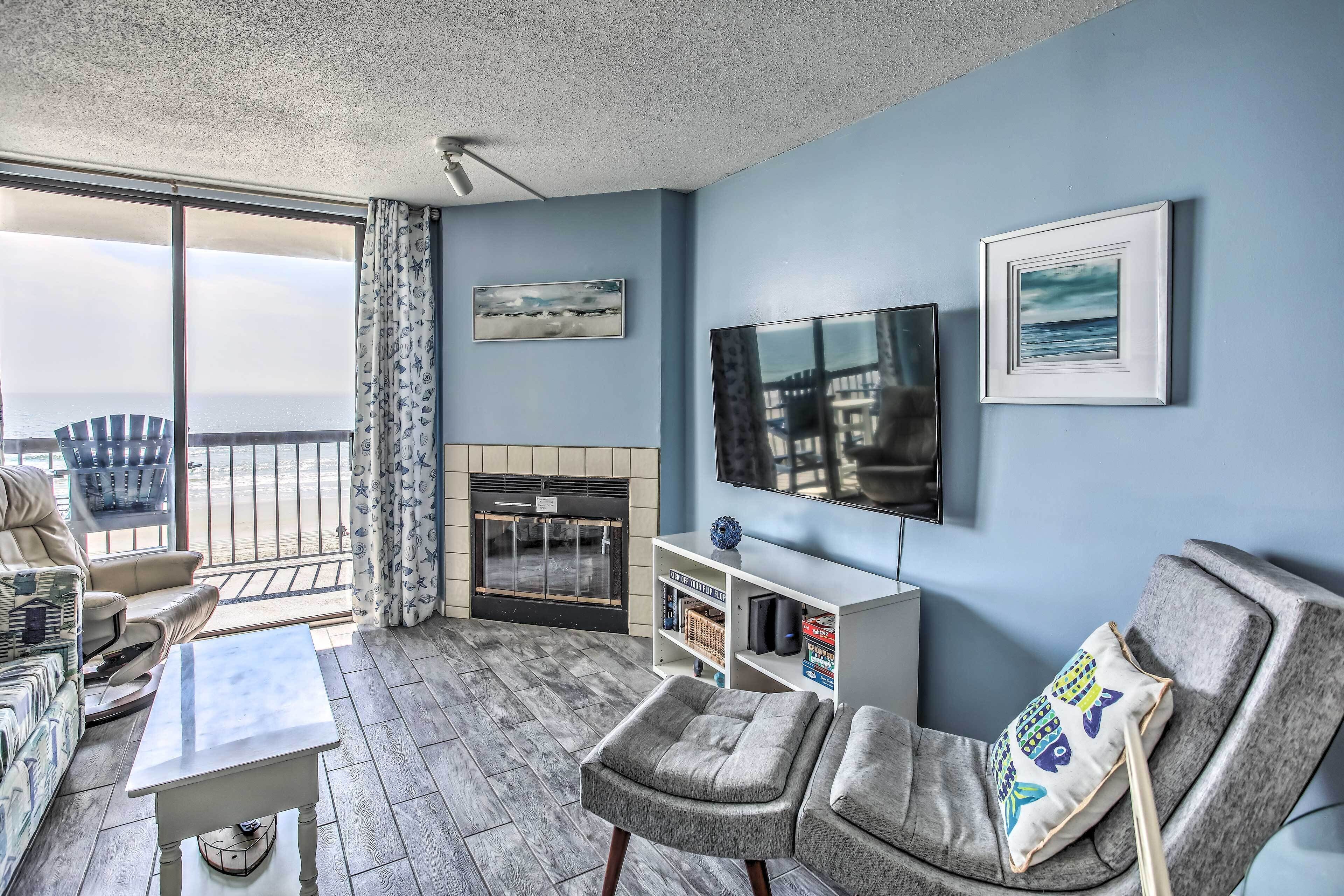 A living room with a fireplace, a television, and a view of the ocean.