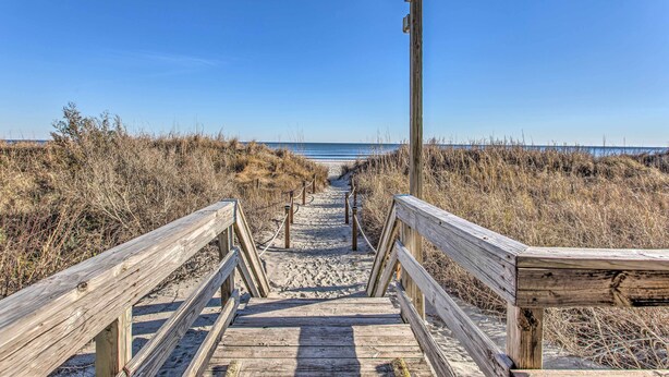 A wooden boardwalk leading to a beach with a clear sky.