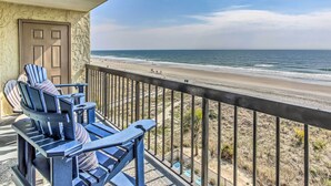 A balcony with a view of the beach, featuring Adirondack chairs and a door.
