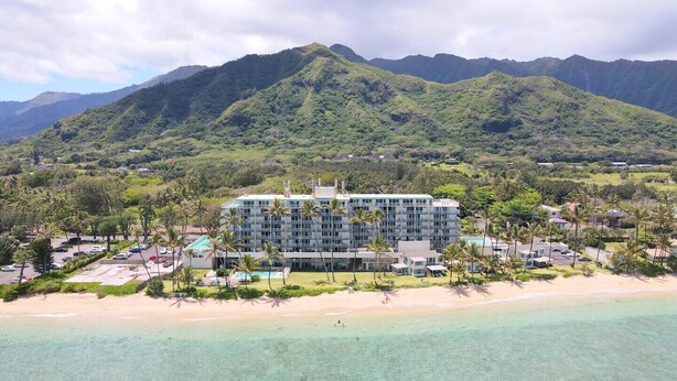 Un resort con un gran edificio, una playa y montañas al fondo.