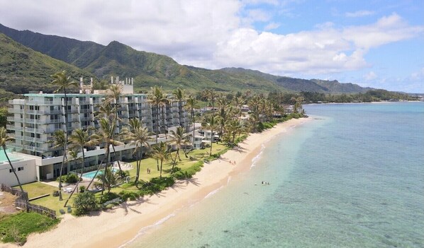 A beachfront hotel with multiple floors, a pool, and palm trees. - Deluxe Beachfront Condo with a breathtaking view (Hauula)