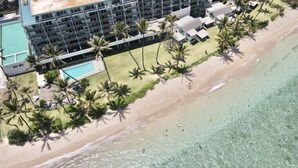 Vista aérea de un hotel frente al mar con varias edificaciones, una piscina y palmeras.