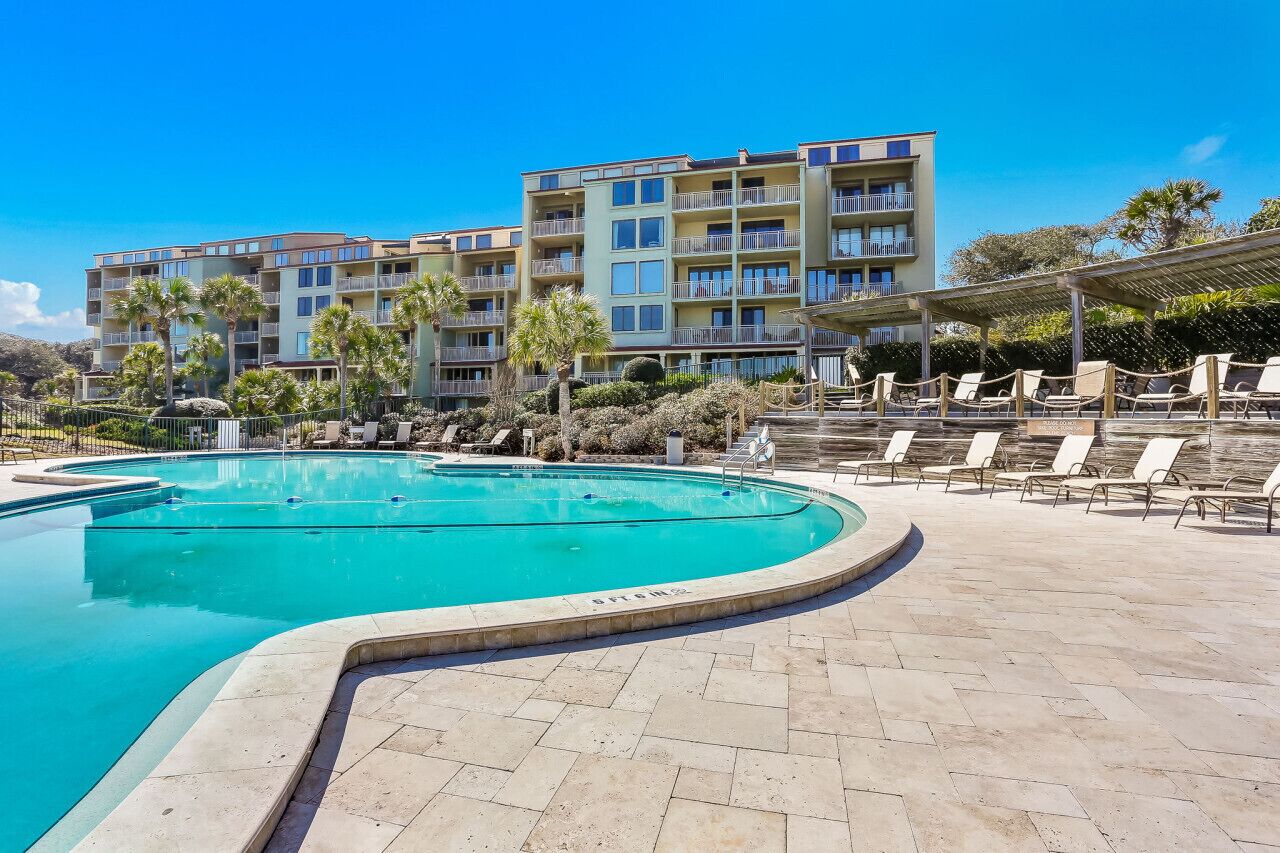 Ein Swimmingpool mit Liegestühlen und im Hintergrund ein Gebäude mit Balkonen.