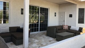 A covered patio area with a brown sectional sofa, wicker chairs, and a small table. - Southwestern Patio Home-Magnificent Mountain Views (Oro Valley)