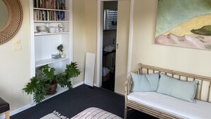 A room with a bookshelf, a painting, a bed, and a potted plant. - Kestrel Place (Ocean Grove)
