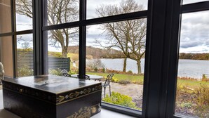 A view through a window of a lake with trees, a patio with chairs, and a decorative box on a table. - Tarn End Cottage 5, Talkin Tarn, ideal for a family, activities and historical sites nearby (BRAMPTON)