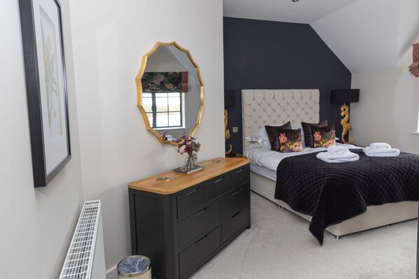 A bedroom with a bed, dresser, mirror, and radiator. - Tarn End Cottage 5, Talkin Tarn, ideal for a family, activities and historical sites nearby (BRAMPTON)