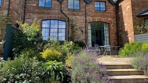 A brick house with a garden, a patio with chairs, and a large arched window. - Tarn End Cottage 5, Talkin Tarn, ideal for a family, activities and historical sites nearby (BRAMPTON)