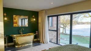 A modern bathroom with a freestanding bathtub, a large mirror, and a view of a lake through a glass door. - Tarn End Cottage 8, Talkin Tarn, Brampton ideal for a romantic break overlooking the Tarn (BRAMPTON)
