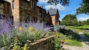 A stone building with a garden in front, a paved path, and a grassy area. - Tarn End Cottage 8, Talkin Tarn, Brampton ideal for a romantic break overlooking the Tarn (BRAMPTON)