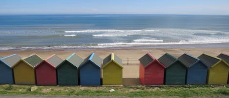 Una hilera de cabañas de playa coloridas a lo largo de una carretera costera, con el océano al fondo.