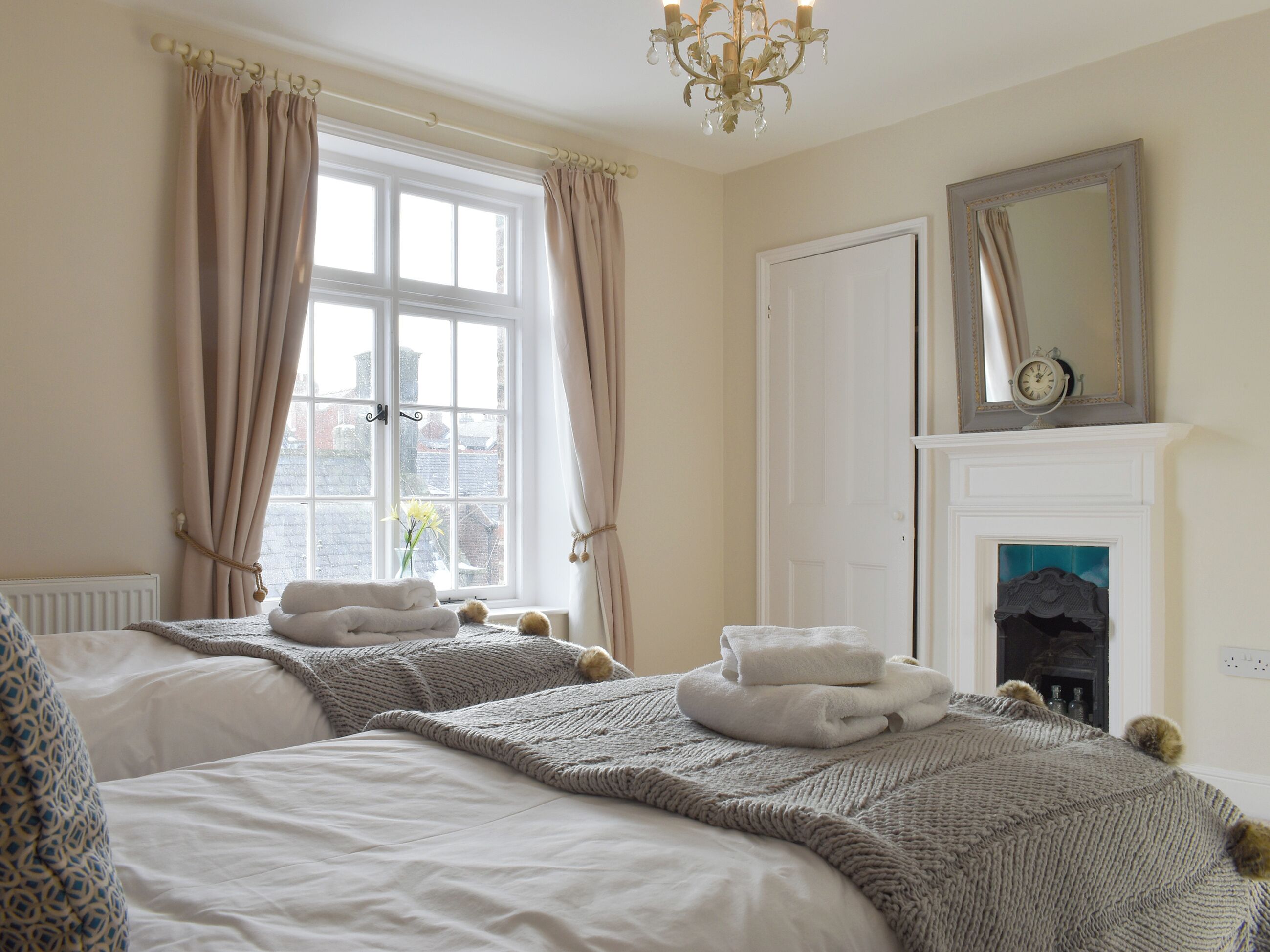 A hotel room with two beds, a fireplace, a window with curtains, and a chandelier.