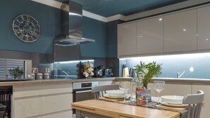 Una cucina moderna con un tavolo da pranzo in legno, mobili bianchi e una cappa aspirante in acciaio inossidabile.