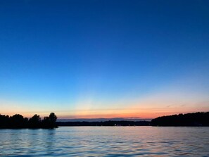 A calm lake at dusk with a clear sky and distant shoreline.