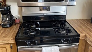 A stainless steel stove top oven with a microwave above it, a coffee maker, and a white towel hanging from the oven door.