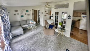 A living room with a sofa, armchair, and coffee table. There is a door leading to a kitchen.