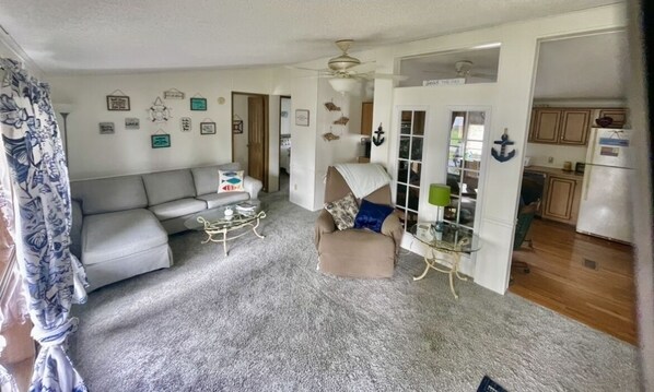 A living room with a sofa, armchair, and coffee table. There is a door leading to a kitchen.