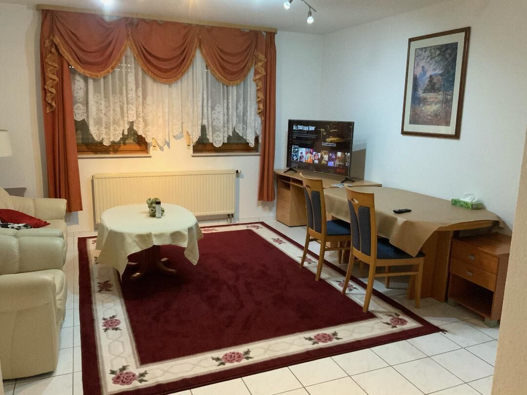 A living room with a sofa, a small round table, a dining table with chairs, a TV, and a radiator.