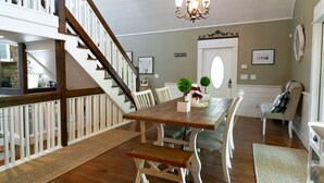 A dining area with a wooden table, white chairs, a bench, a staircase, and a chandelier. - Coosawattee-2 King Beds, Hot Tub, Pool Table, Fire Pit, Arcade, Resort Amenities (Ellijay)