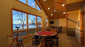 Una habitación amplia con mesa de billar, telescopio y ventanas grandes que dan a una vista del lago.