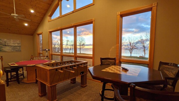 Una habitación acogedora con mesa de fútbol de mesa, un tablero de ajedrez y grandes ventanales con vistas a un lago pintoresco.