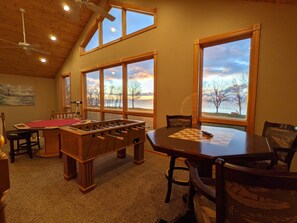 A cozy room with a foosball table, a chessboard, and large windows overlooking a scenic lake. - Mille Lacs Family Getaway (Aitkin)