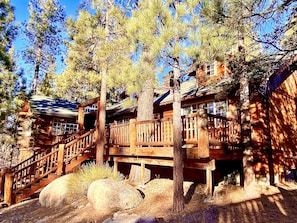 A wooden cabin with a wooden staircase leading to a deck, surrounded by pine trees. - Enchanted Log Home on Large Lot Pet friendly (Big Bear Lake)