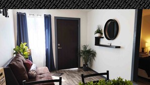 A modern living room with a brown leather sofa, a dining table with chairs, a black-framed mirror, and potted plants. - The White Bungalow (Rosarito)