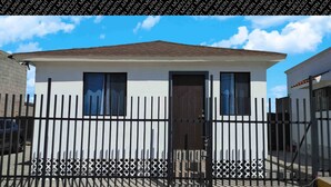 A modern two-story building with a flat roof, a black metal fence, and a gated entrance. - The White Bungalow (Rosarito)