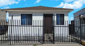 A two-story house with a black metal fence, a wooden door, and two windows. - The White Bungalow (Rosarito)