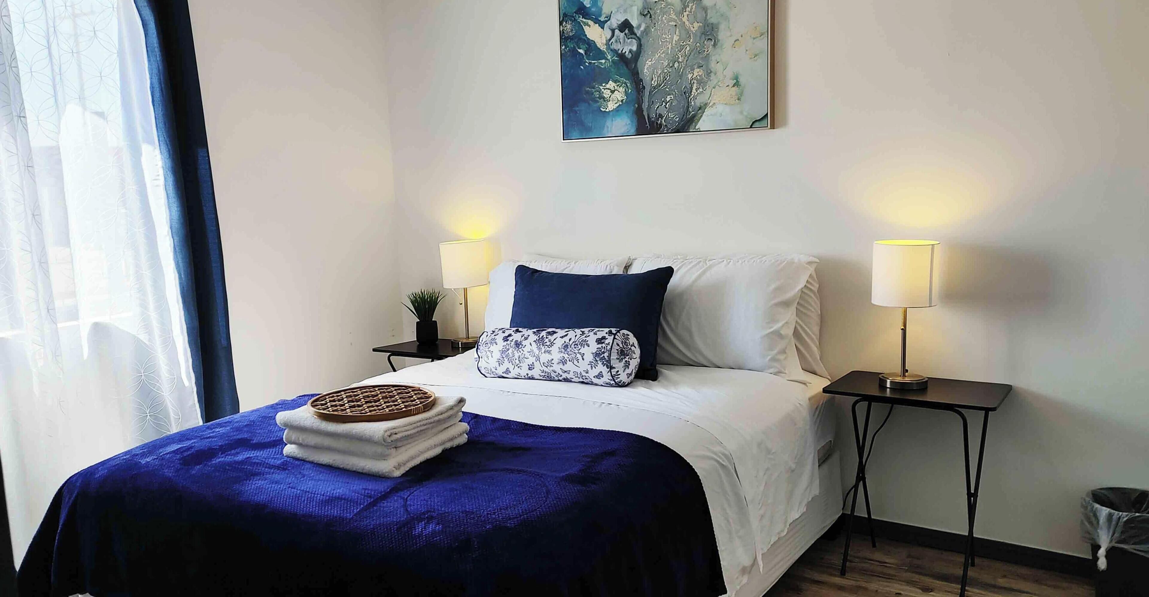 A neatly arranged bedroom with a bed, two bedside tables, a lamp, and a painting on the wall.