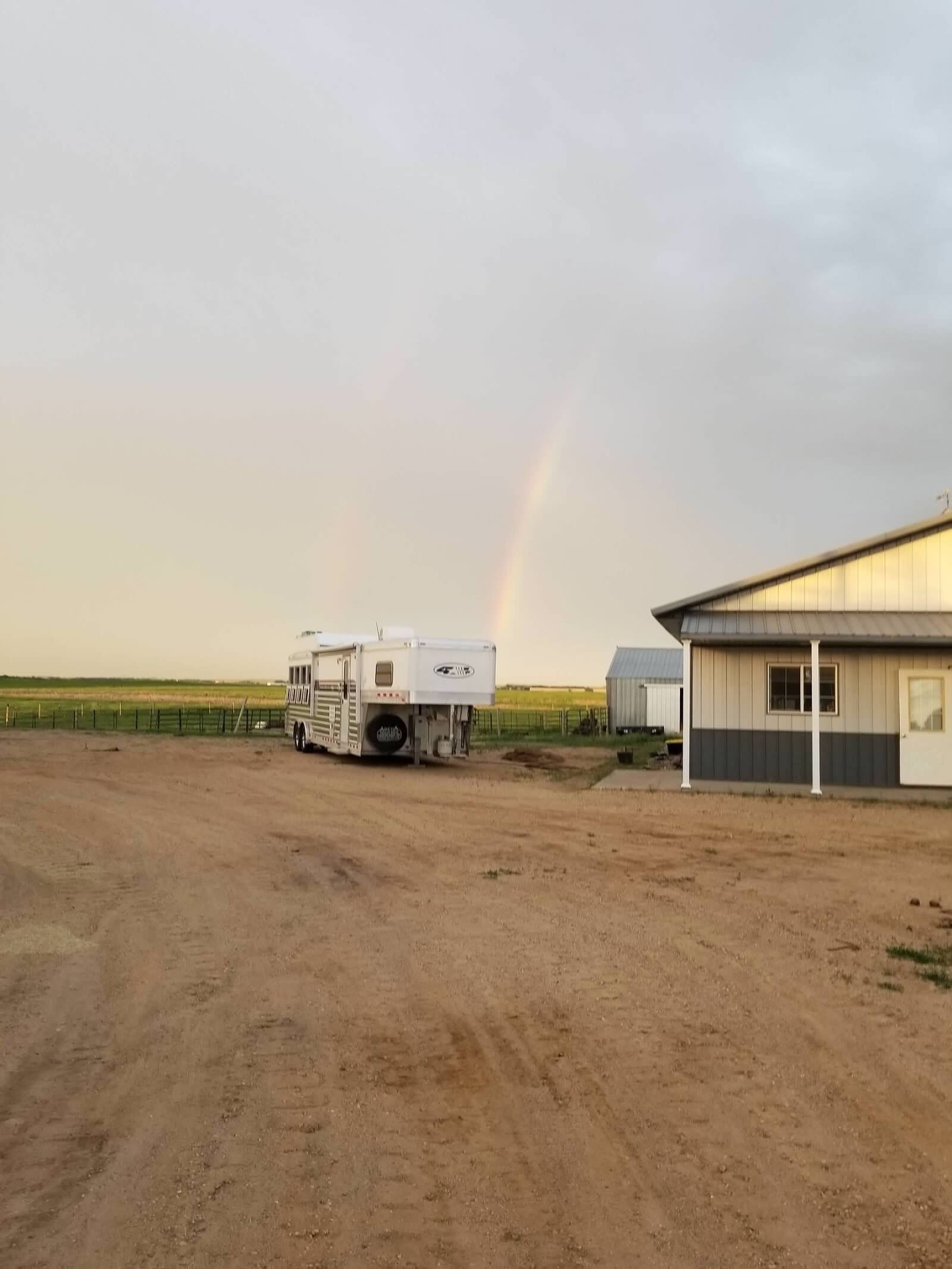 A trailer parked in a dirt lot with a building and a fence in the background.