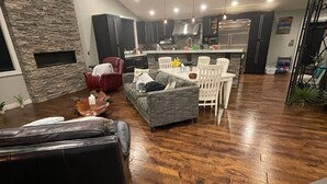 A modern living room with a stone accent wall, a leather sofa, a gray sofa, and a dining area with white chairs.