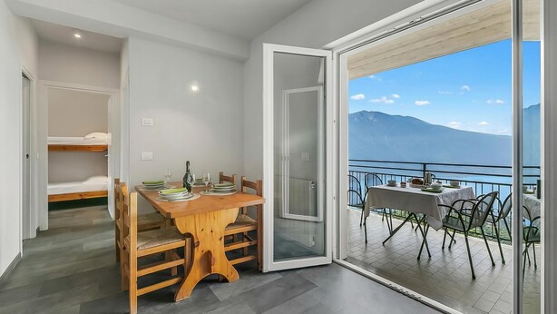 A modern room with a wooden dining table, chairs, a bed, and a balcony with a view of mountains.
