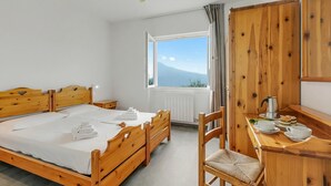 A wooden bed with a view of a mountain, a wooden desk with a kettle, and a chair.