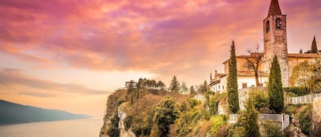 A historic building with a bell tower, situated on a cliff overlooking a body of water.