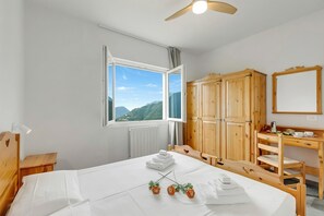 Une chambre à coucher avec un lit, des meubles en bois, un bureau, un miroir et une fenêtre donnant sur la montagne.