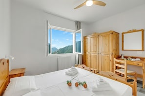 Ein Schlafzimmer mit Bett, Holzschrank, Schreibtisch und Fenster mit Blick auf die Berge.